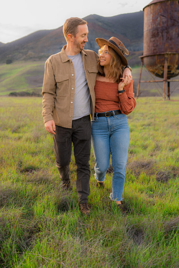 Couple embracing beside a rustic water tower with mountains in the background in Clayton, California