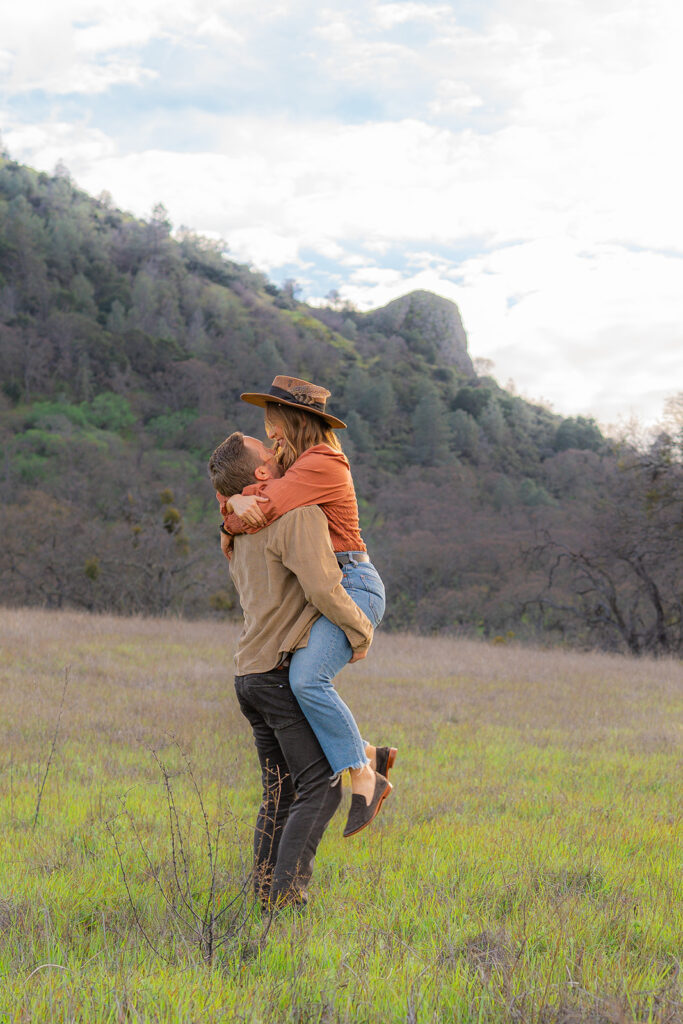 Couple embracing in an open field near a rustic water tower and Mt. Diablo in the Bay Area