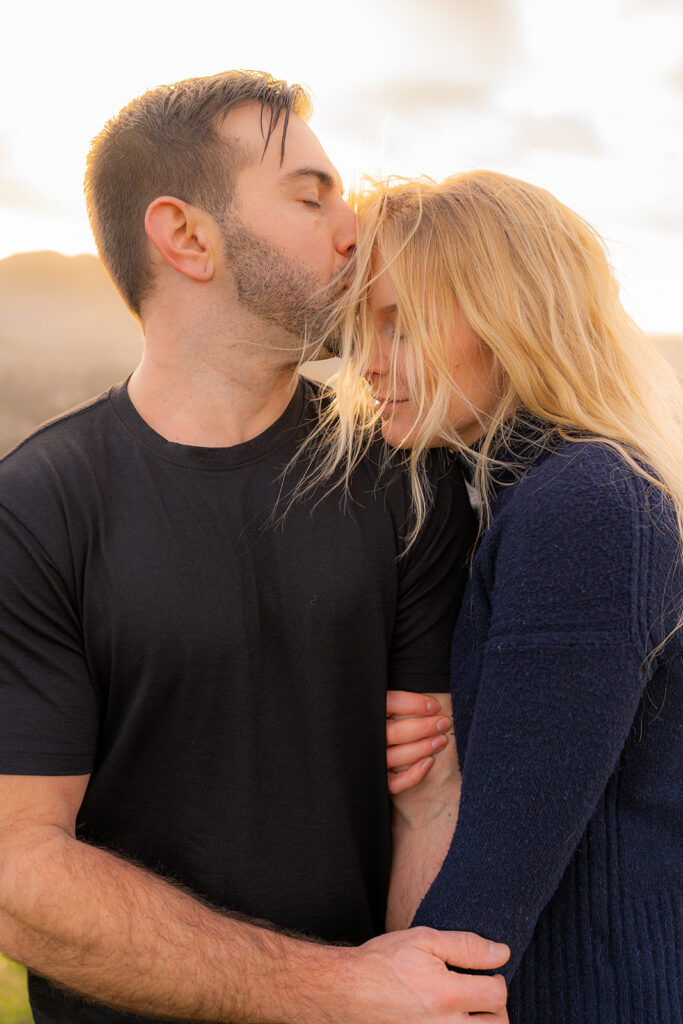 Couple sharing a tender forehead kiss with sweeping mountain views in the background in California