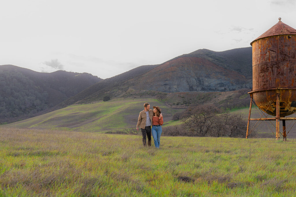 Modern-styled couple posing beside a rustic water tower with mountains in the background in Clayton, California
