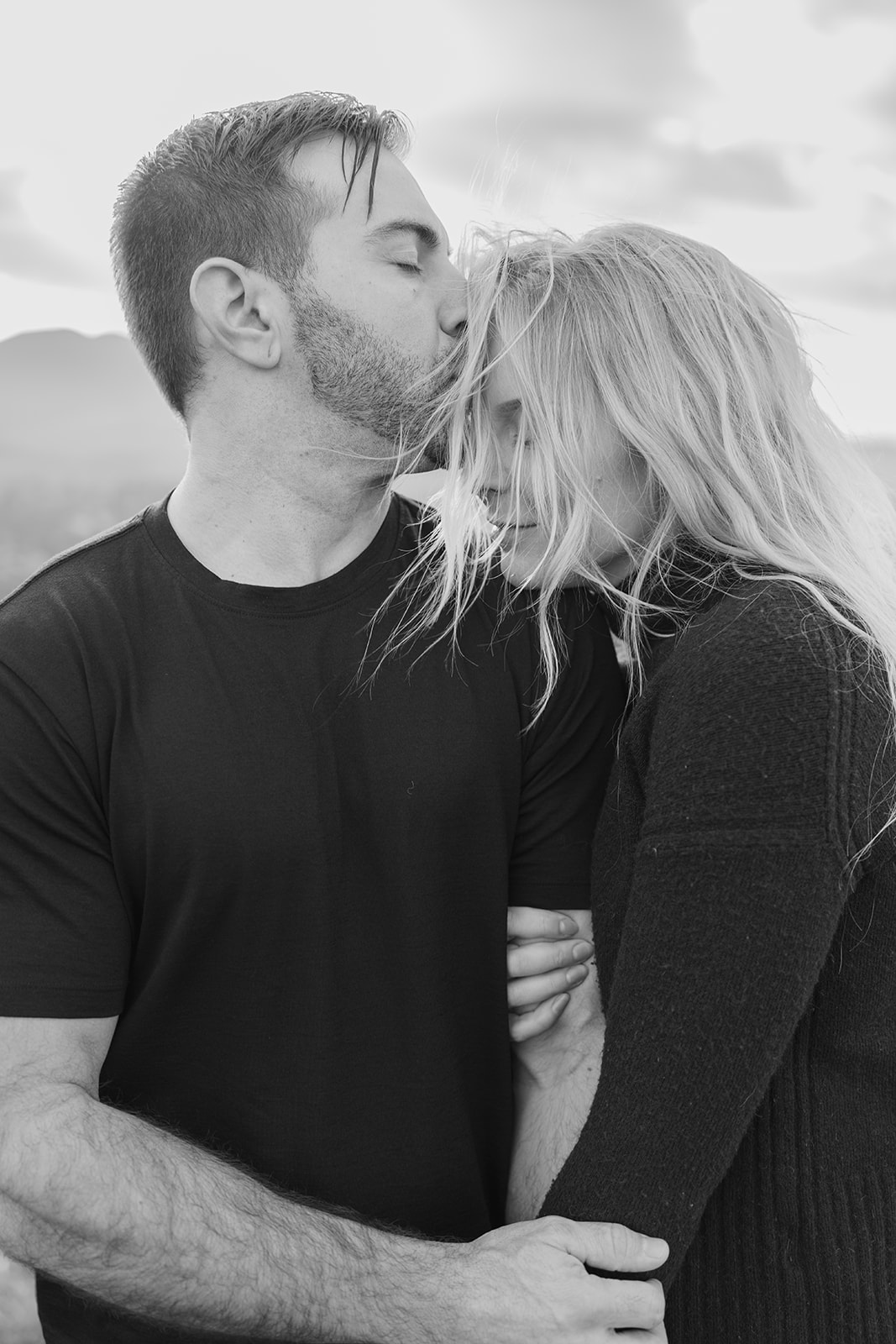 One partner gently kissing the other’s forehead with a mountain landscape in the background in California